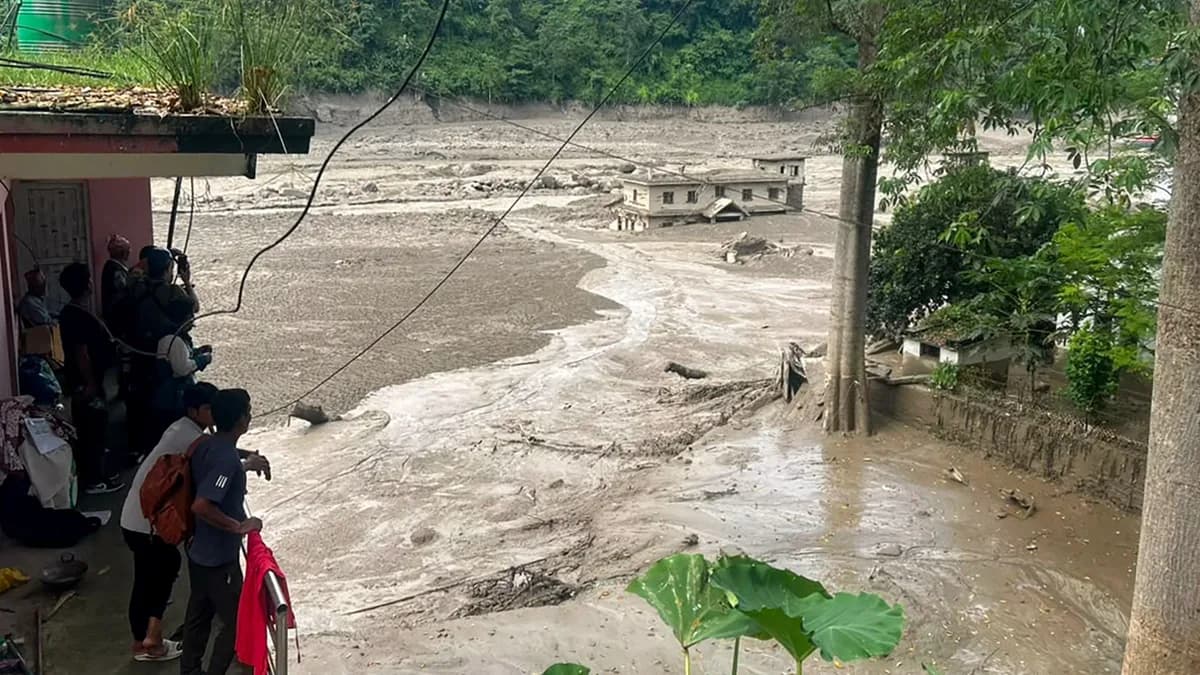 Aftermath of a massive flash flood in a mountainous region of Nepal, with mud covering buildings while residents look on
